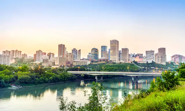 Edmonton city skyline at sunrise with the river and bridge in the foreground.