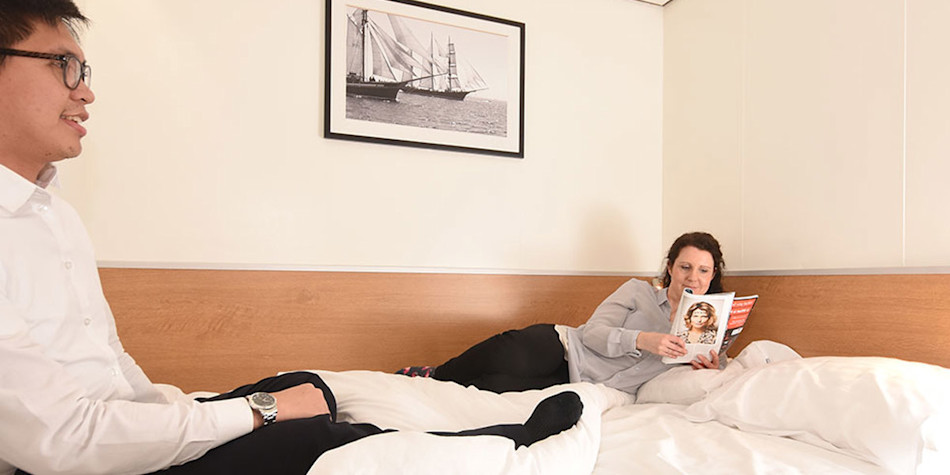 Two friends relaxing and reading magazines on the bed in a double bed cabin