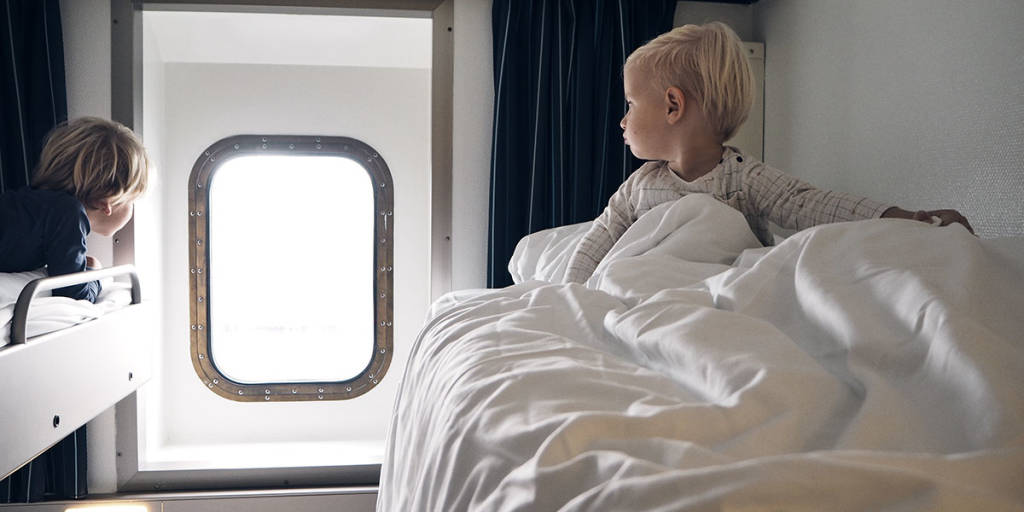 Dwójka dzieci siedzi na piętrowym łóżku i patrzy przez okno w kabinie promu