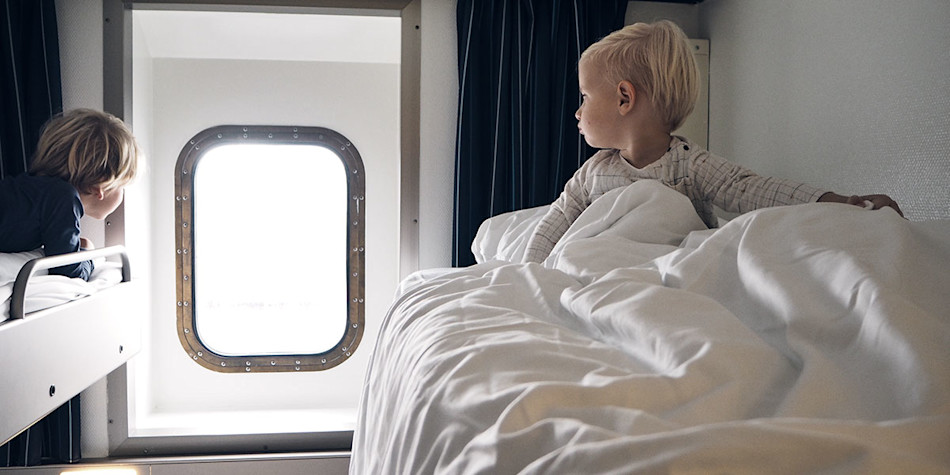 Two children on the top bunks of the sea view cabin are peering out of the window 