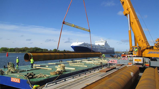 DFDS employees loading pipes on a barge with a DFDS ship in the background