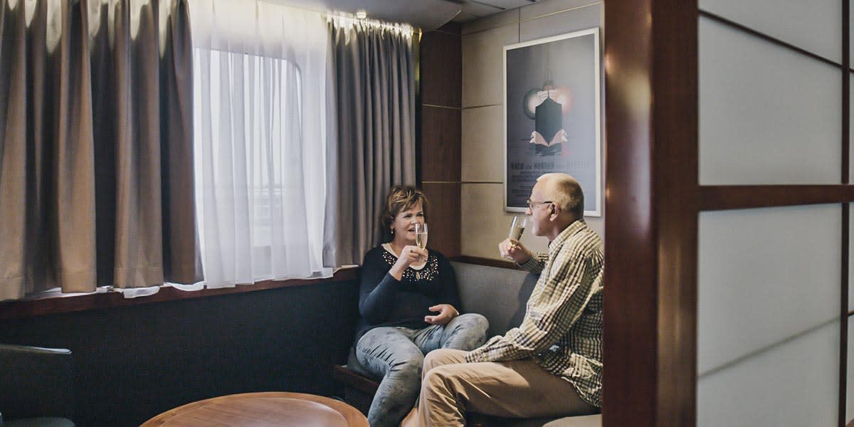Starsza para siedzi na sofie w luksusowej kabinie Commodore i pije szampana