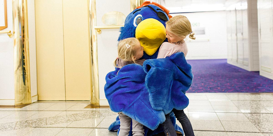 Two children being hugged by an onboard entertainer/mascot dressed up as a giant bird. 