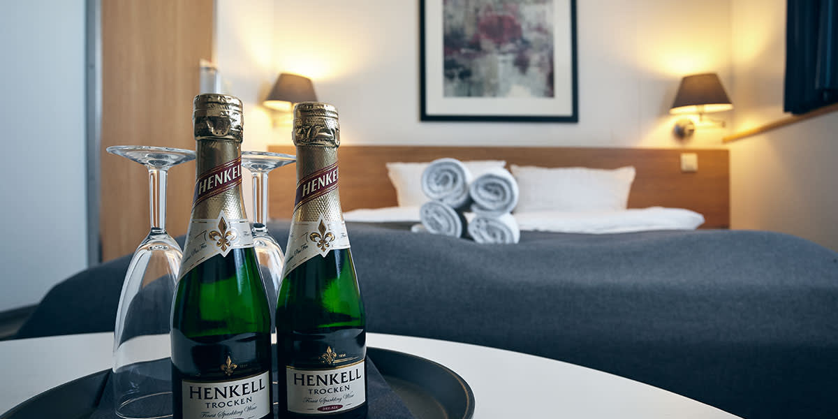 Zbliżenie na dwie małe butelki szampana i kieliszki, w tle widać łóżko