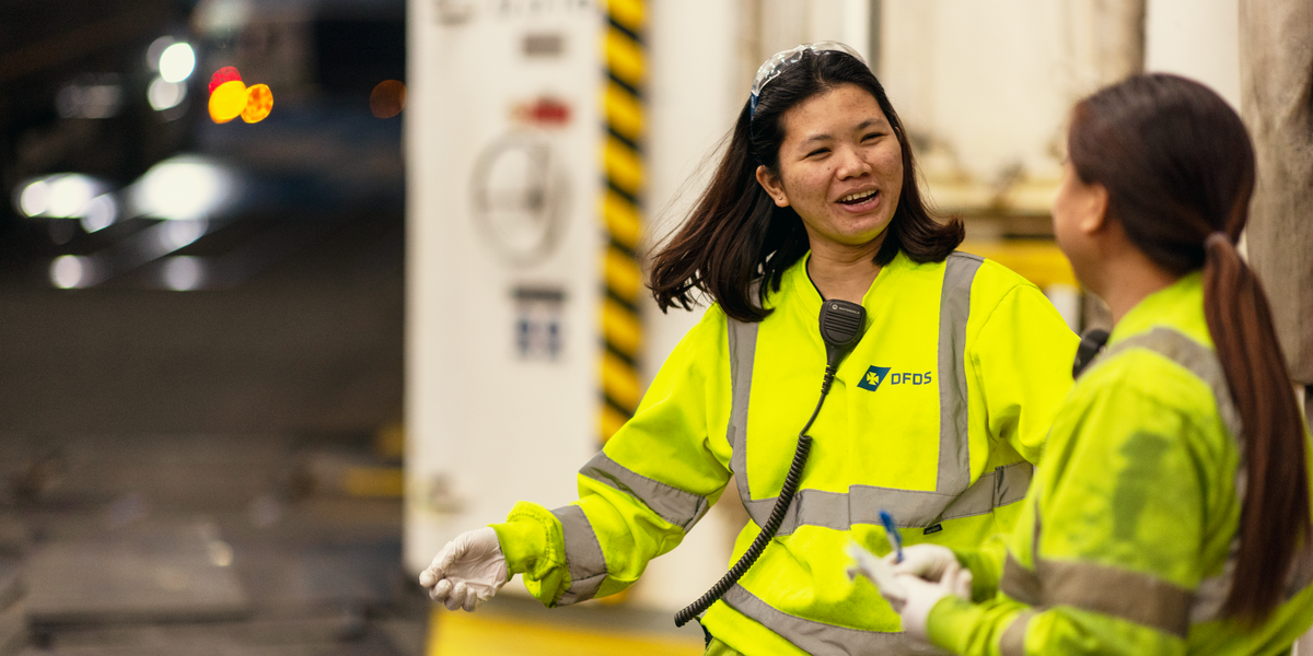 Two female DFDS seafarers on a vessel, wearing yellow security clothing, talking to each other 5C0A1780 - link box About index page - Caring employer