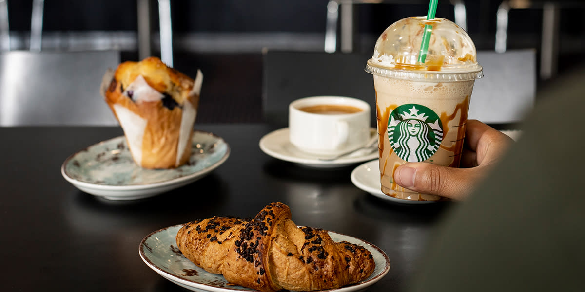 Croissant, babeczka i kawa w kubku Starbucks na stole