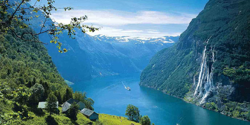 Fjord on a sunny day in Norway. A waterfall in running down into it and a boat is on the water.