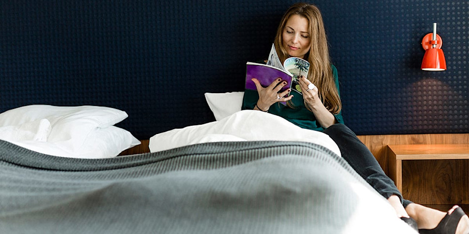 Woman reading a magazine on a double bed in a commodore de luxe cabin.