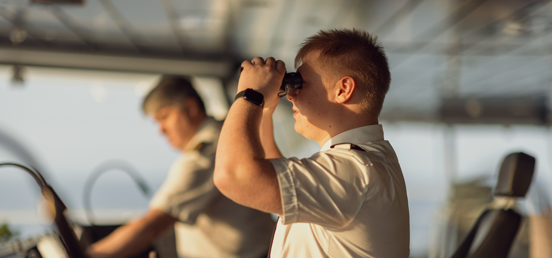 Seafarer at the bridge of a DFDS' vessel, one of them looking through binoculars at sea in the distance 5C0A7121 (1920x900px) AHV - Q2 Report 2025