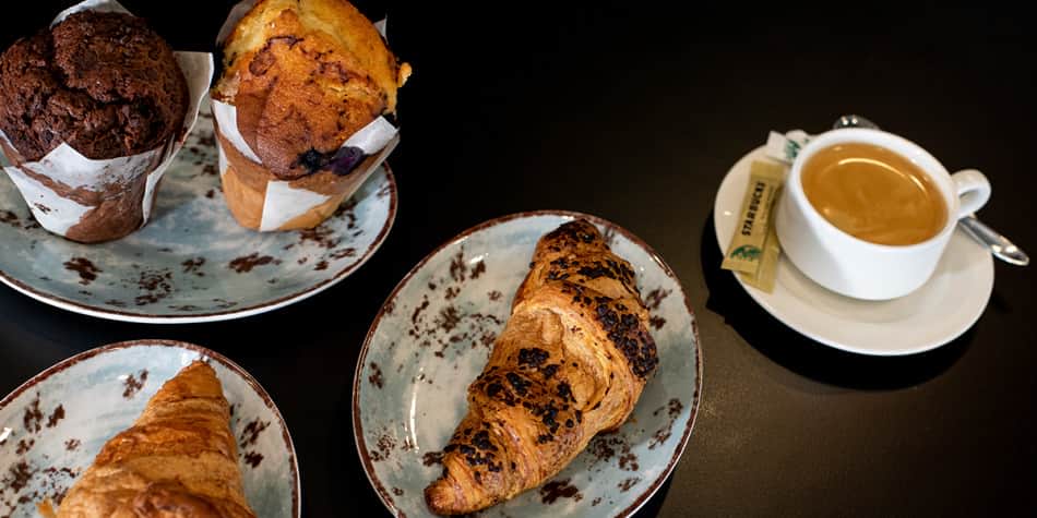Kaffee, Croissant und Muffins auf dem Tisch