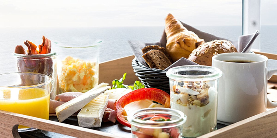 A selection of breakfast options (such as yogurt, croissants, bacon) on a tray. 