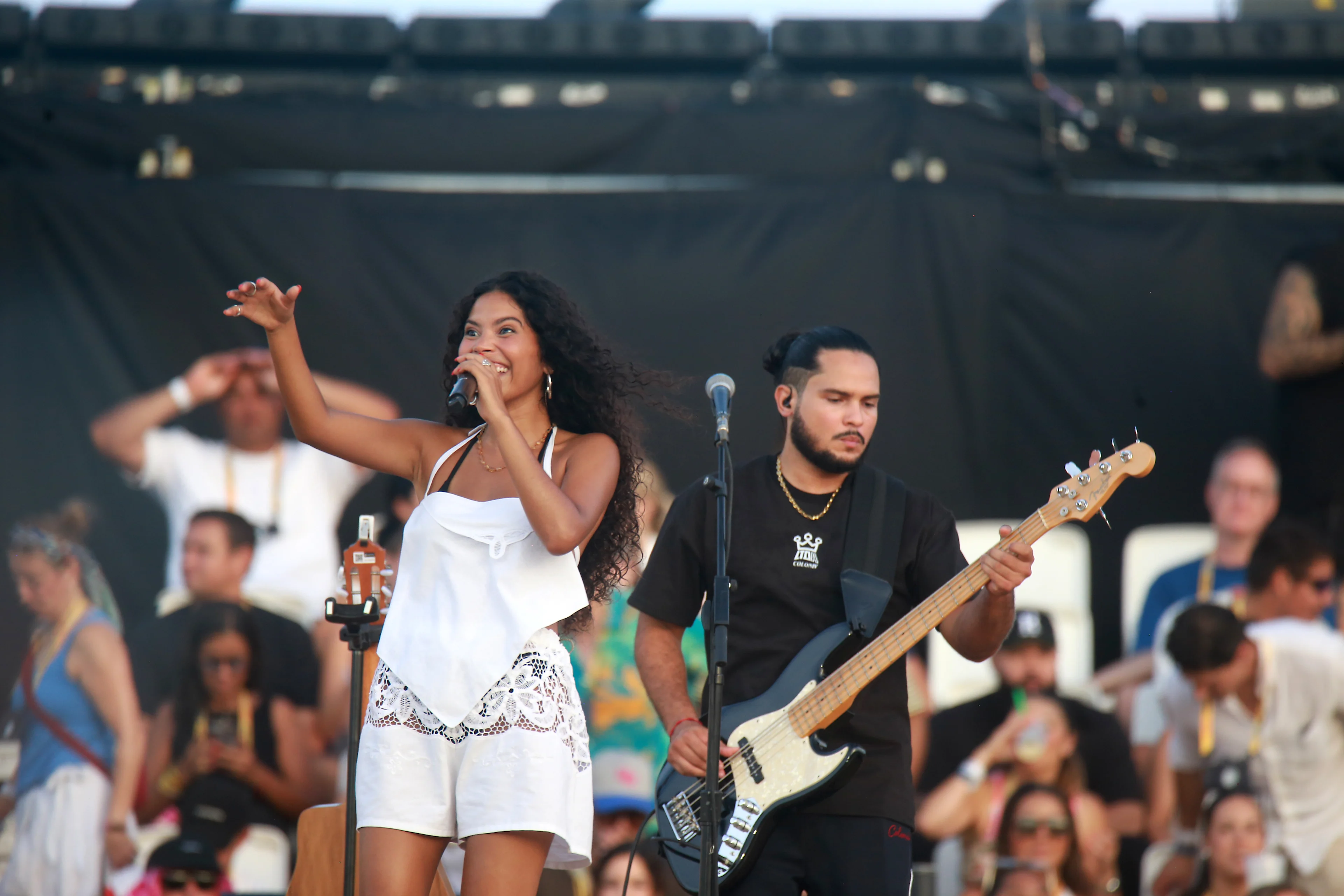 Cantante con vestido blanco y bajista en concierto al aire libre frente a público numeroso al atardecer
Gladys Vega/Getty Images