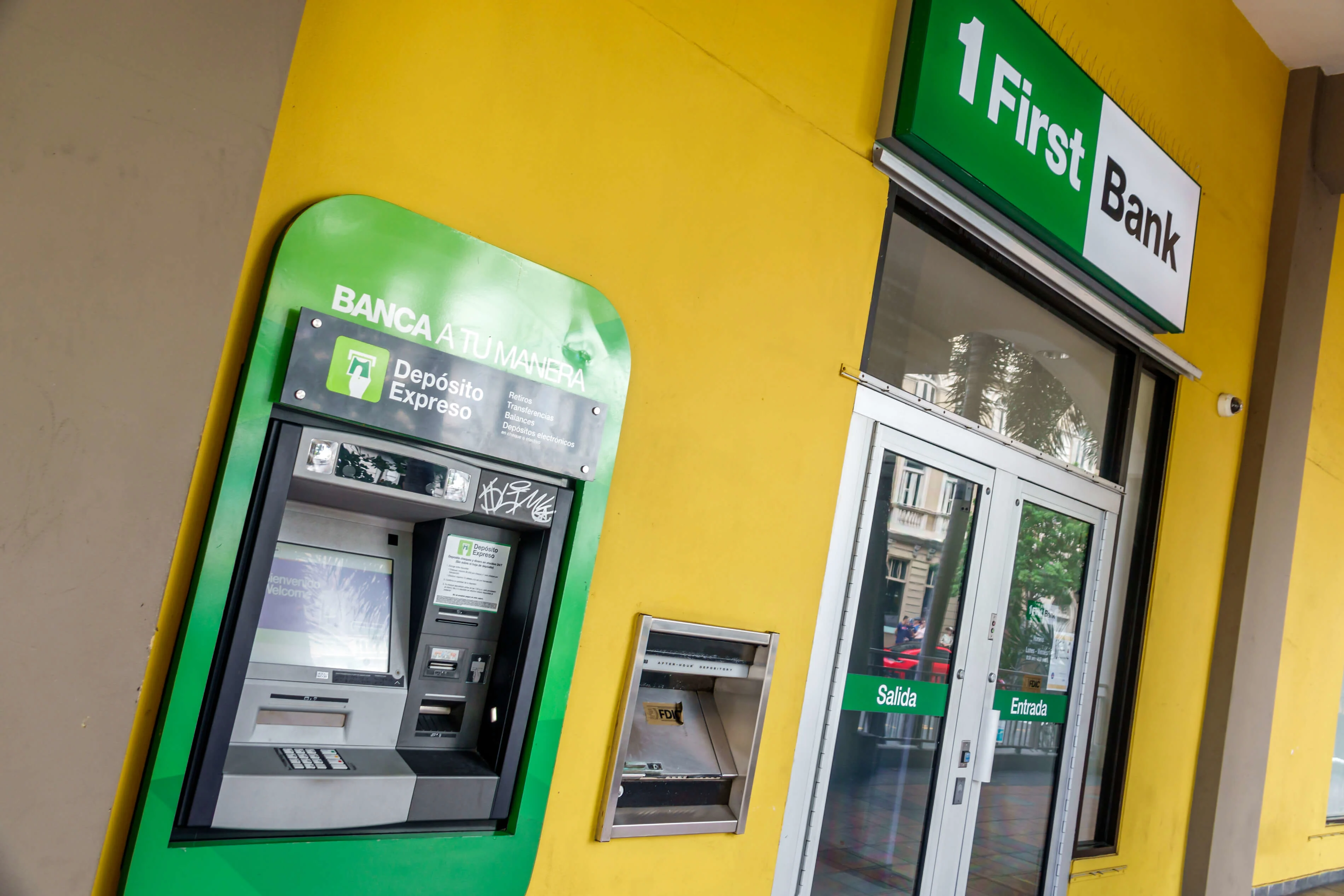 Fachada amarilla de FirstBank con cajero automático verde de depósito expreso y puertas de entrada y salida.

Foto: Jeffrey Greenberg/Universal Images Group via Getty Images