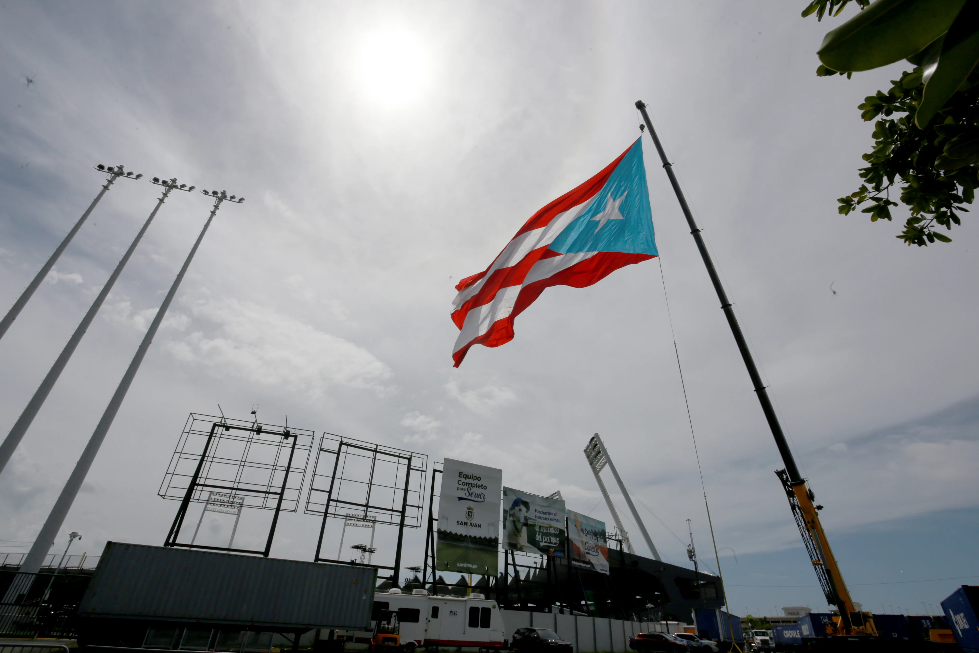 Bandera de Puerto Rico ondeando en un estadio bajo cielo nublado con postes de luz y vallas publicitarias al fondo.
Gladys Vega/Getty Images