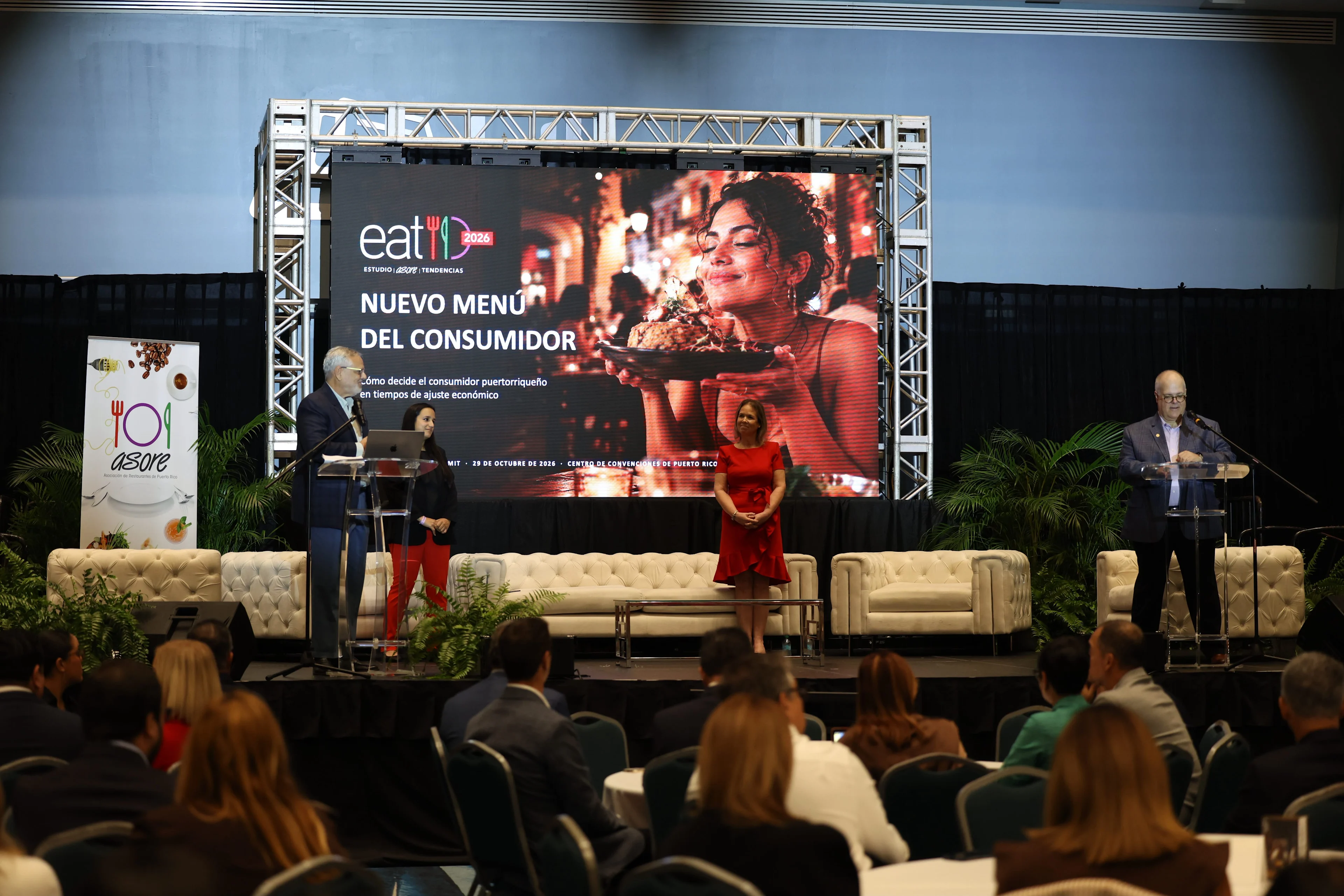 Presentación del evento Eat It 2025 con pantalla que lee Nuevo Menú del Consumidor y tres panelistas en tarima.