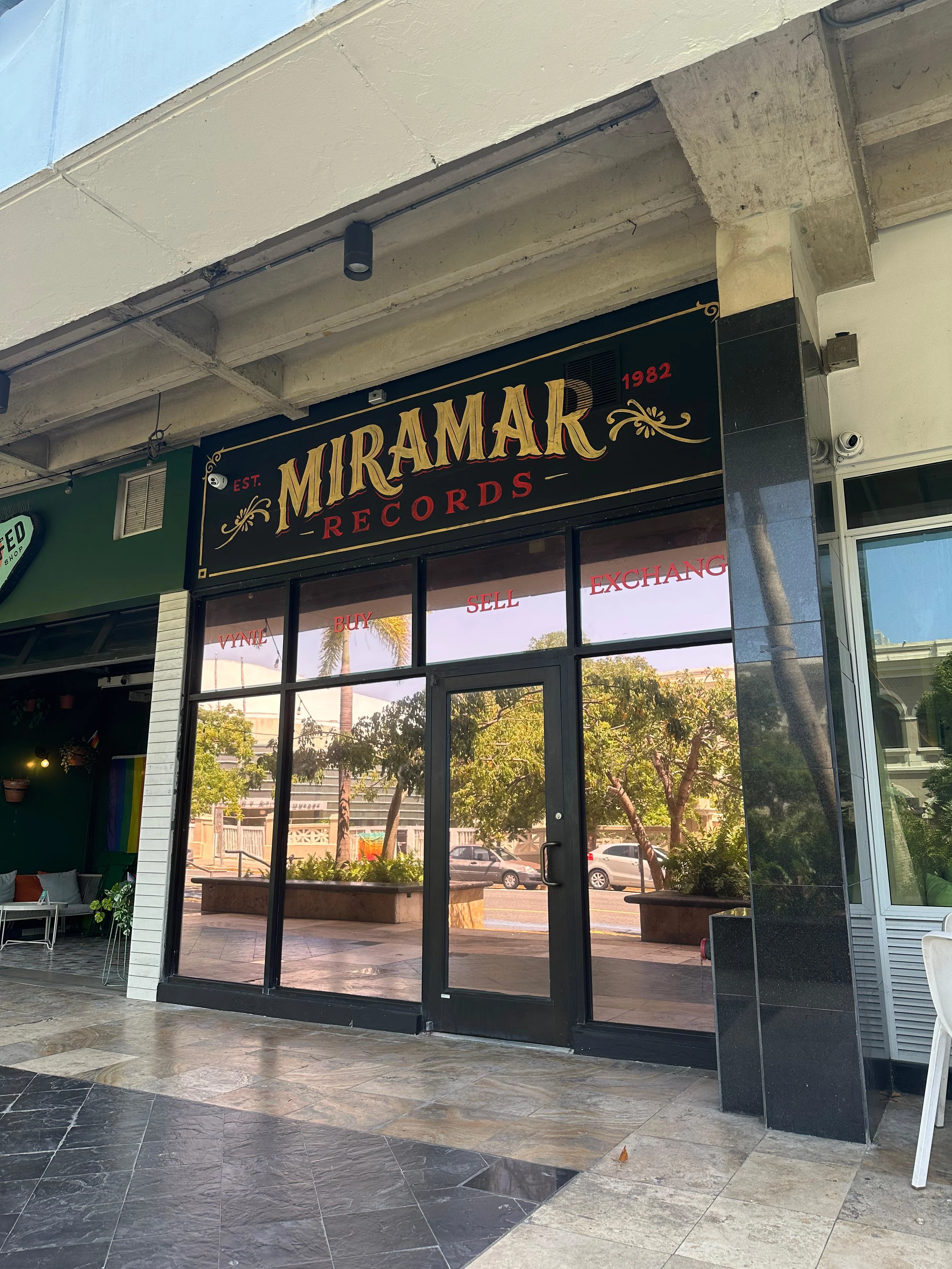 Fachada de Miramar Records con letrero dorado y negro que dice "EST. 1982", puertas de cristal y vista a la calle.
