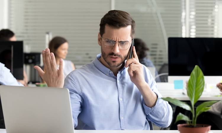 Foto af vred medarbejder, der sidder ved et skrivebord og taler i telefon