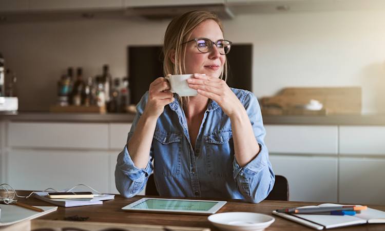 Person sidder i køkken med kaffe i hånden og kigger ud af vindue