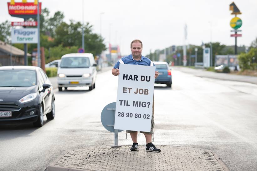 Daniel Jensen står ved en vej med et skilt, hvorpå det står, at han søger job