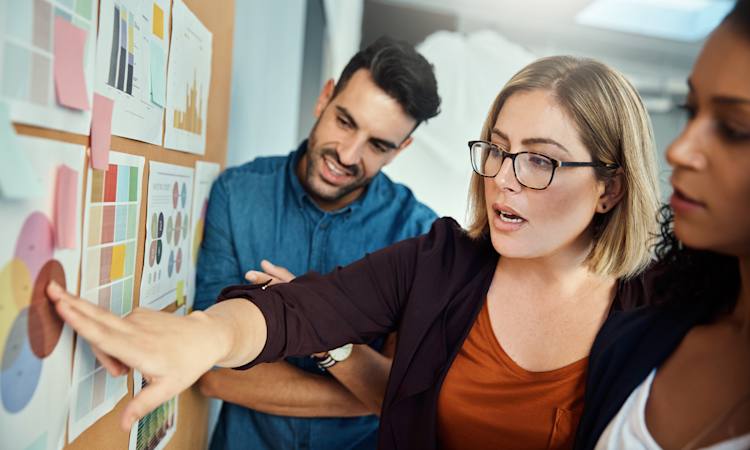 Leder og to kolleger i dialog foran tavle med diagrammer
