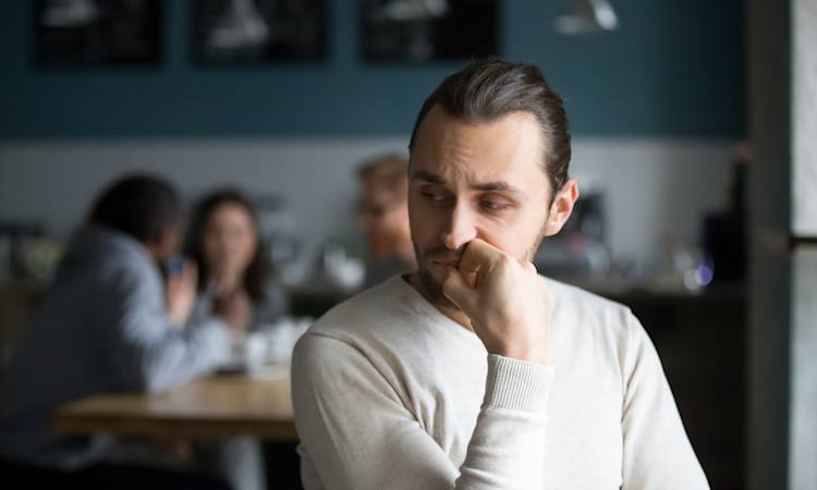 Foto af mand, der er tydeligt tynget af den konfliktsituation, som han står i med de kollegaer, der sidder i baggrunden