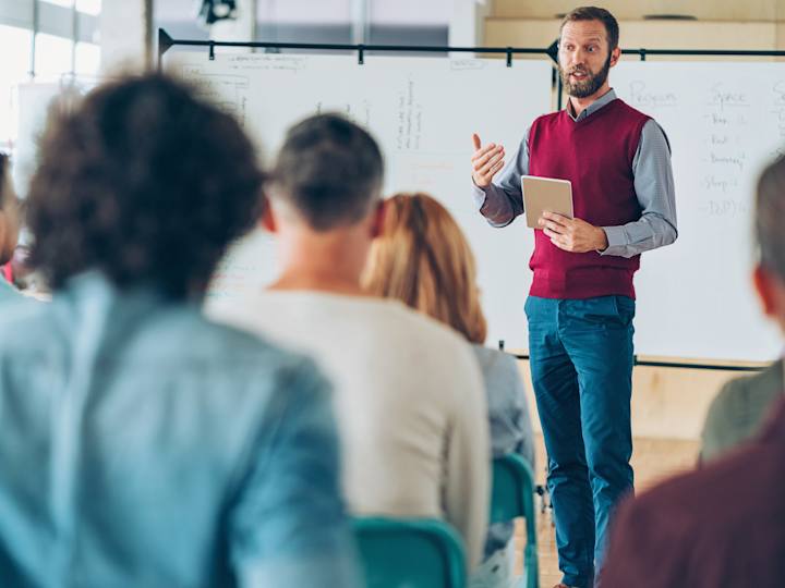 Foto af en kursussituation med stående oplægsholder og siddende kursusdeltagere
