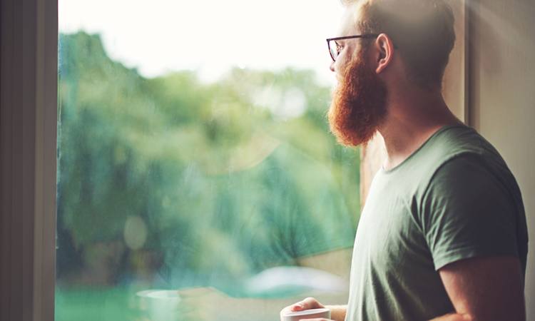 Person sygemeldt med stress kigger ud af vindue fra hjemmet