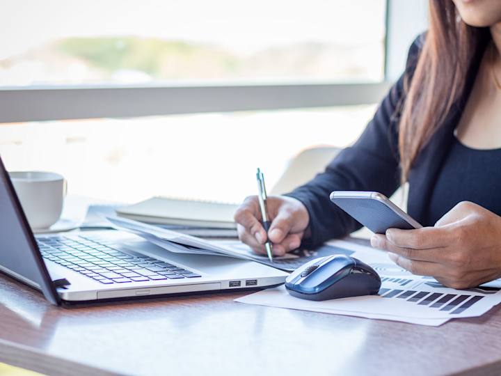 Kvinde ved computer med mobiltelefon og pen i hånden