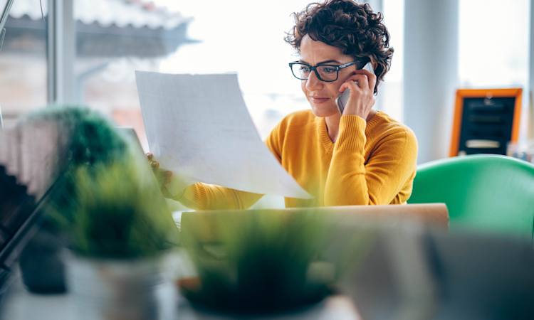 Kvinde på et kontor taler i telefon og kigger på et ark papir