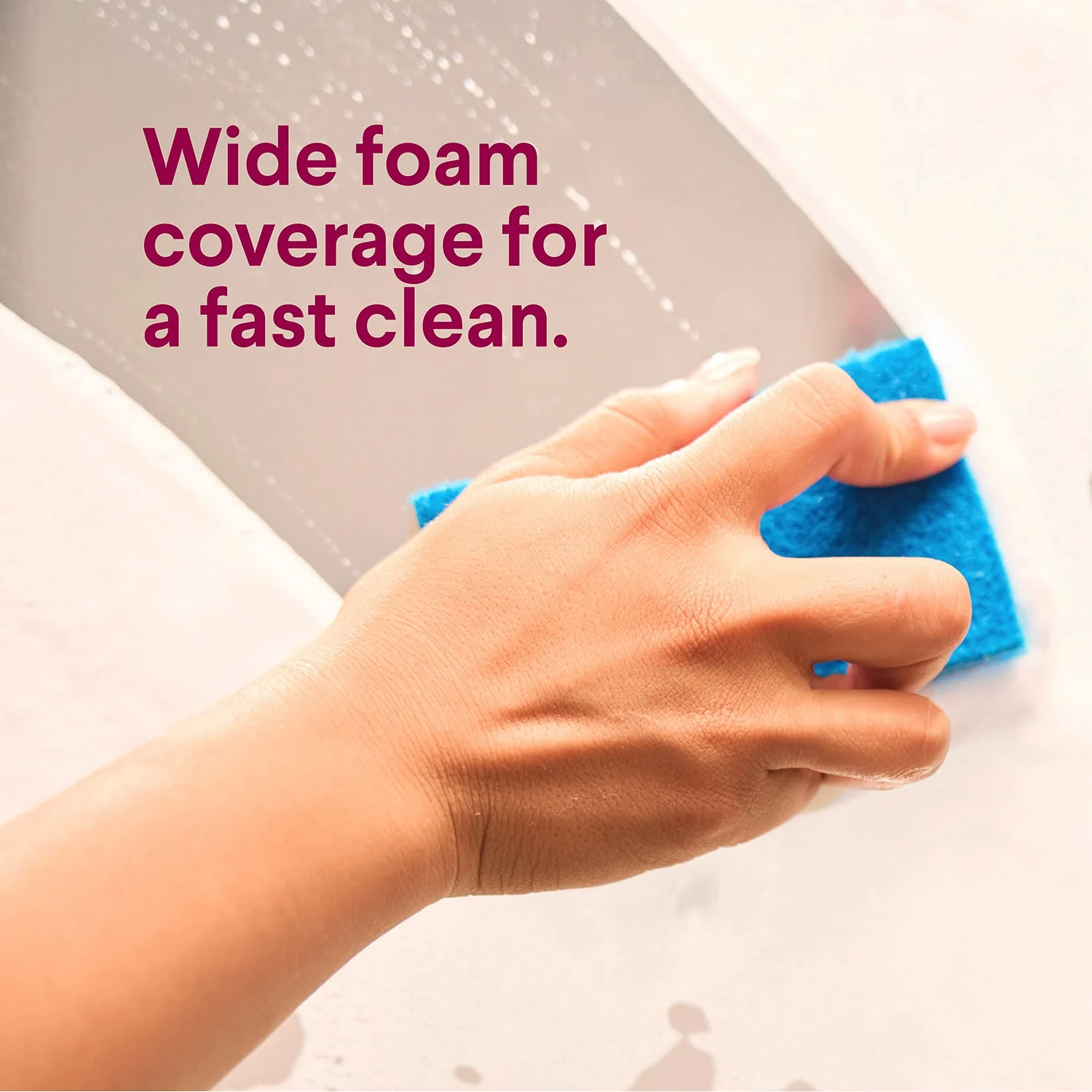 Una mano limpiando una pared sucia con una esponja azul, y las palabras "espuma de amplio alcance para una limpieza rápida"