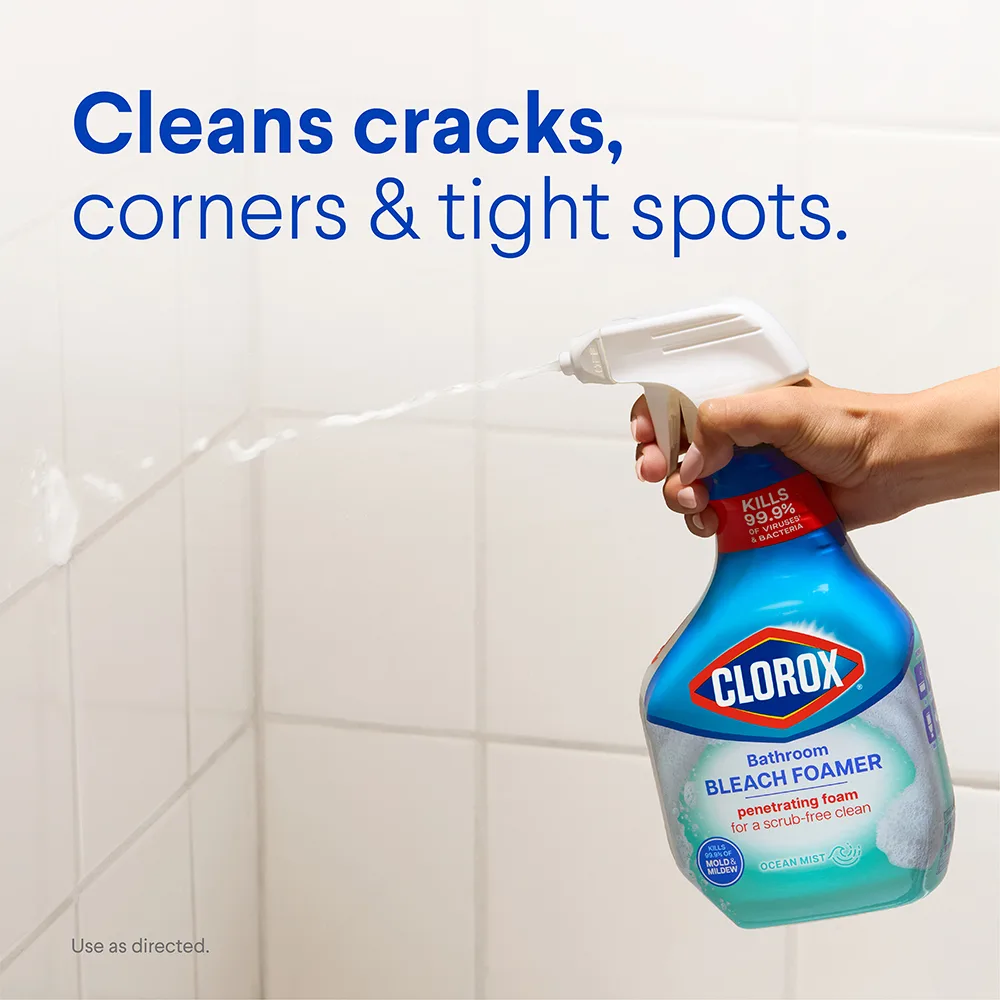 Hand spraying Clorox Bathroom Bleach Foamer on white shower tile, with text: Cleans cracks, corners & tight spots.