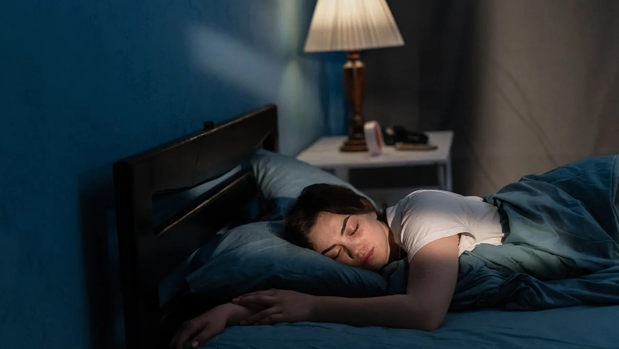 Young woman sleeping in soft bed in late at night. Lying cozily in bed, hugging a pillow.