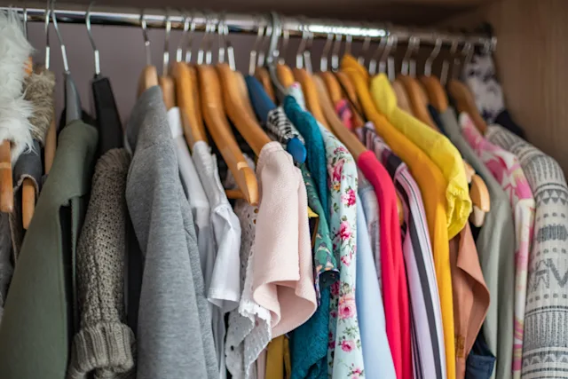 A closet tightly packed with colorful women's clothing on wooden hangers.