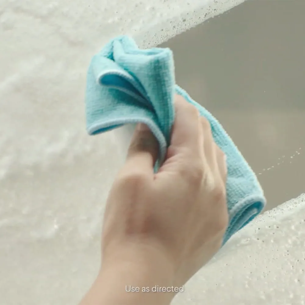 Una mano con un paño azul limpiando espuma del vidrio.