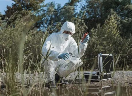 hombre con un traje de protección química tomando una muestra de agua