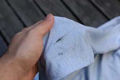 Mano sosteniendo una tela de color azul claro con pequeñas manchas negras sobre una cubierta de madera.