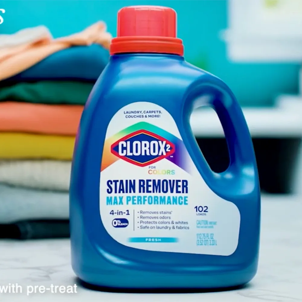 Blue Clorox 2 stain remover bottle with red cap in front of stacked colorful laundry items