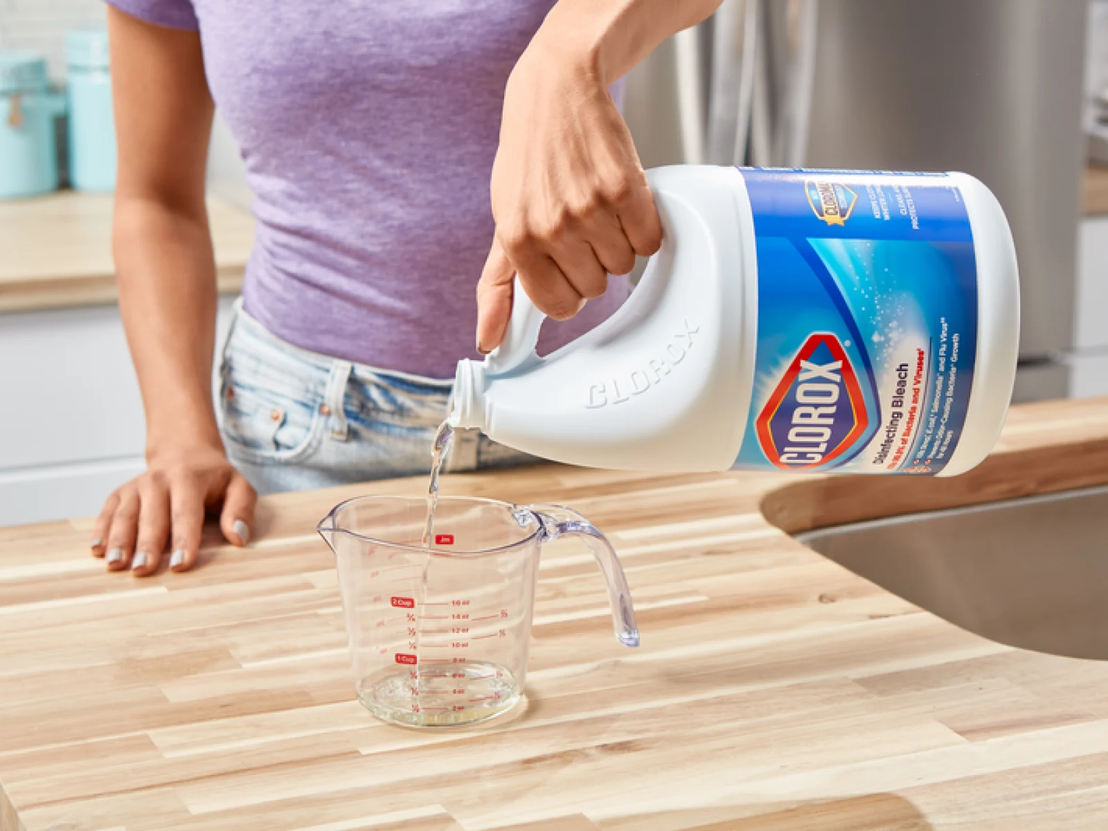 woman pouring Clorox bleach into a measuring cup on a wood countertop