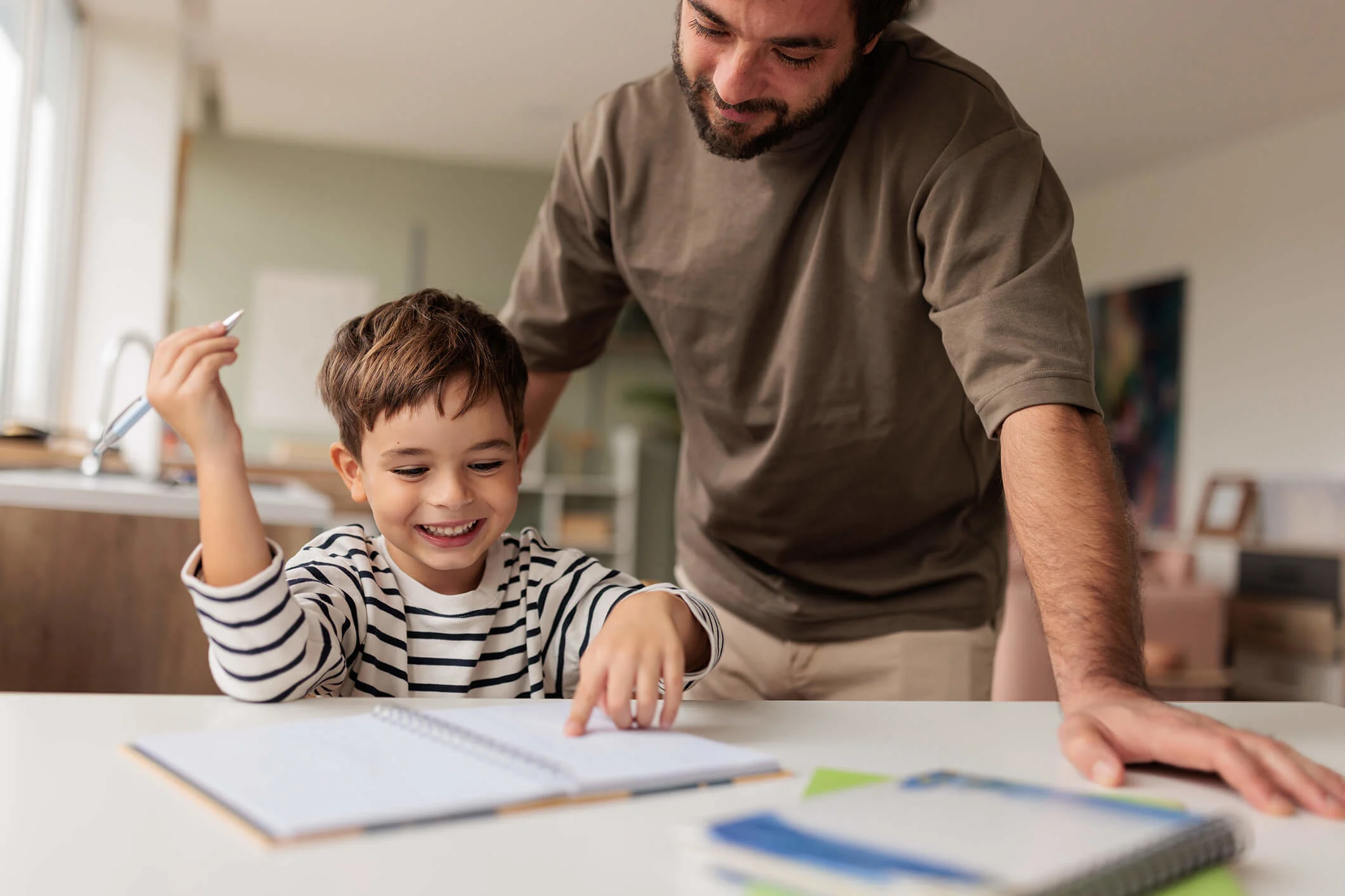 Man helping a young boy with his homework sitting at a kitchen table