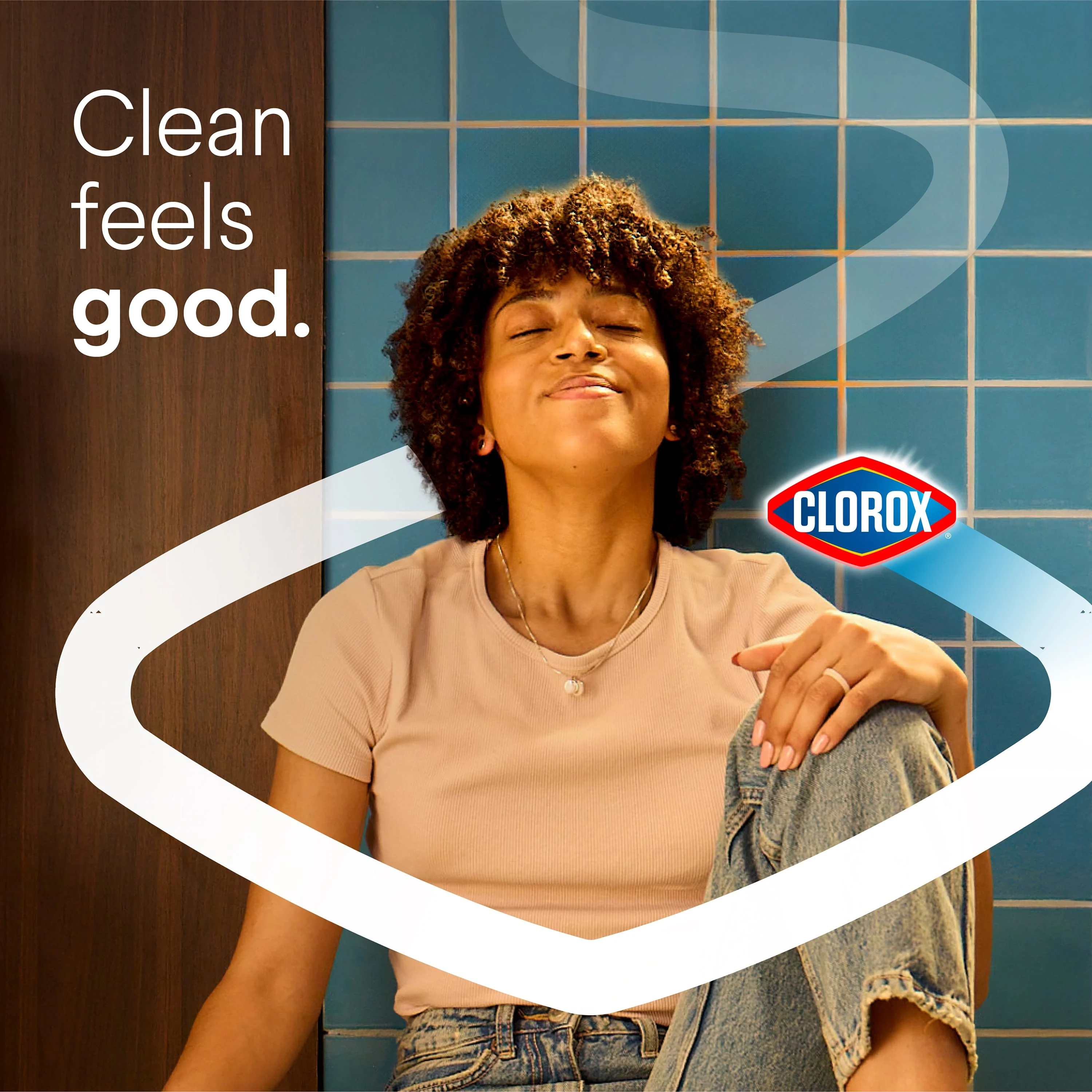 Woman sitting in a bathroom smelling her clean bathroom with a Clorox chevron and the words Clean Feels Good surrounding her