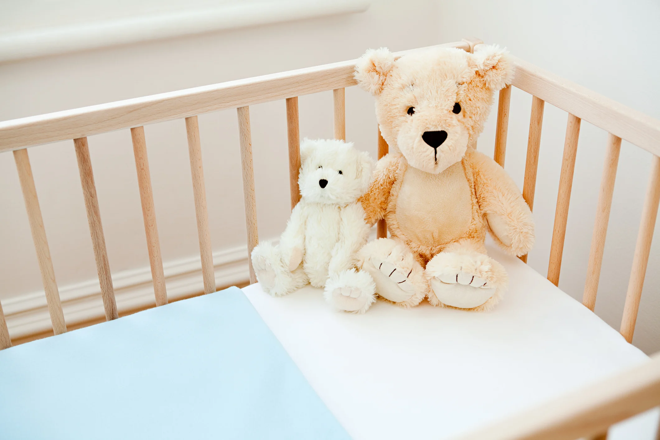 Dos ositos de peluche marrón y blanco sentados en una cuna de madera con ropa de cama blanca y azul.