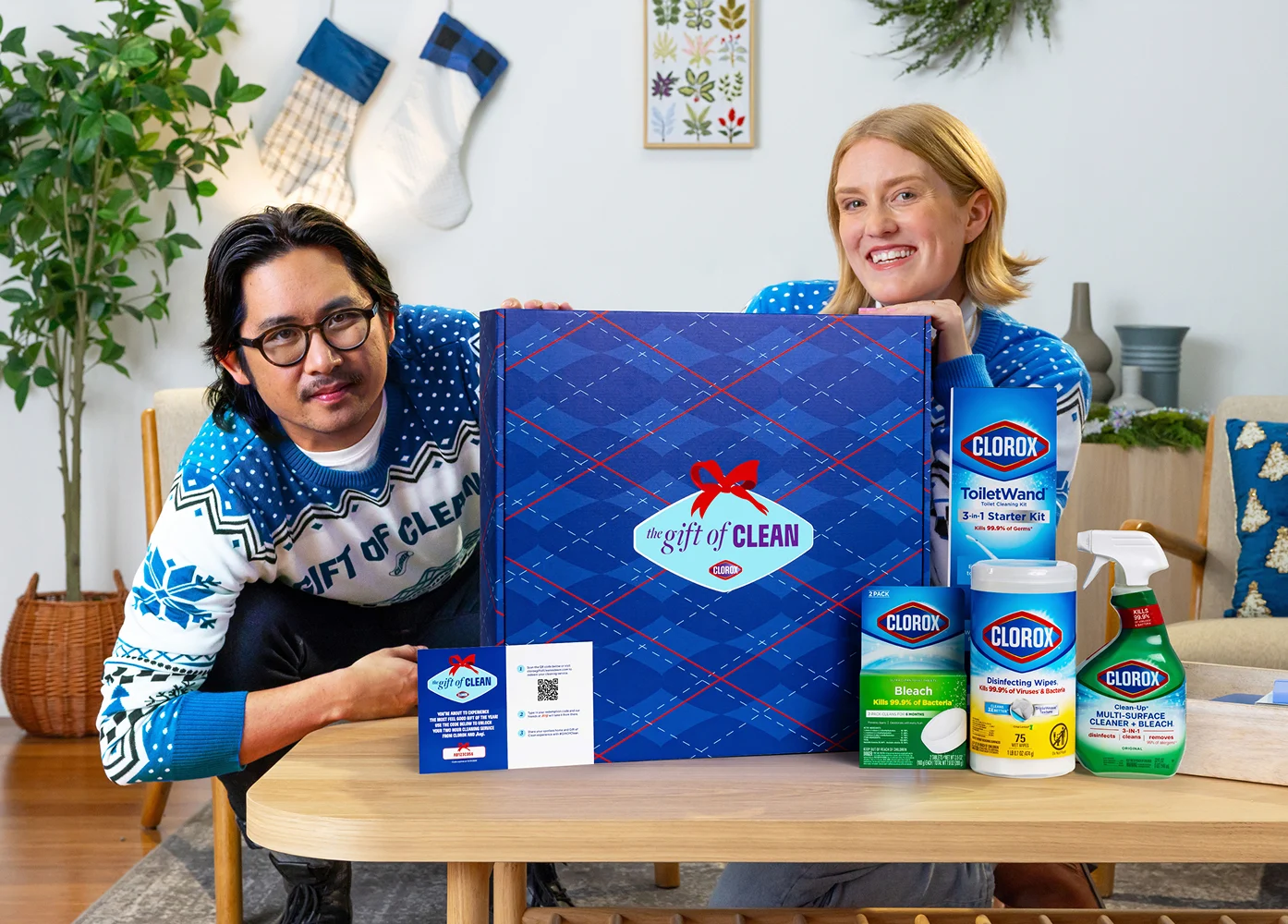 Two people in holiday sweaters sitting on a couch with The Gift of Clean box on a coffee table