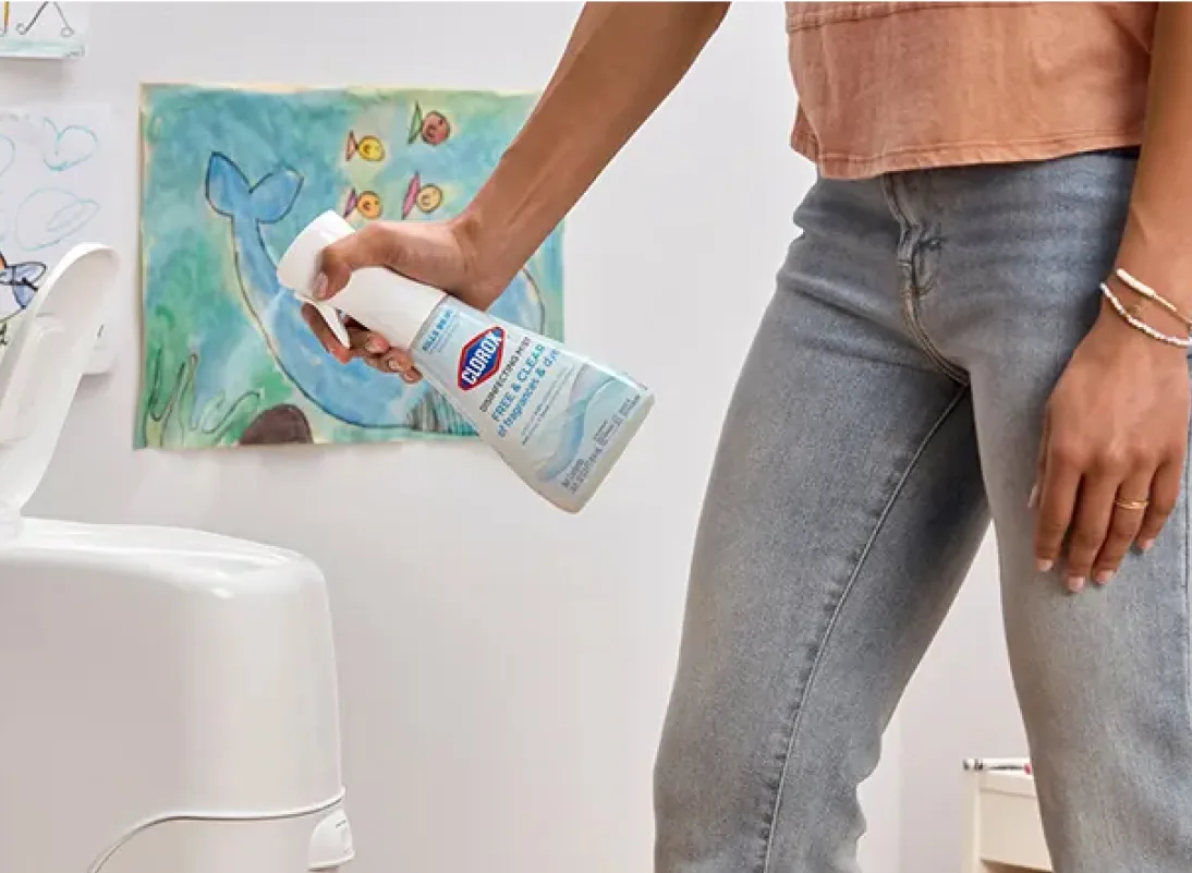 woman spraying a diaper pail with clorox disinfecting bleach. children's drawings on the wall behind