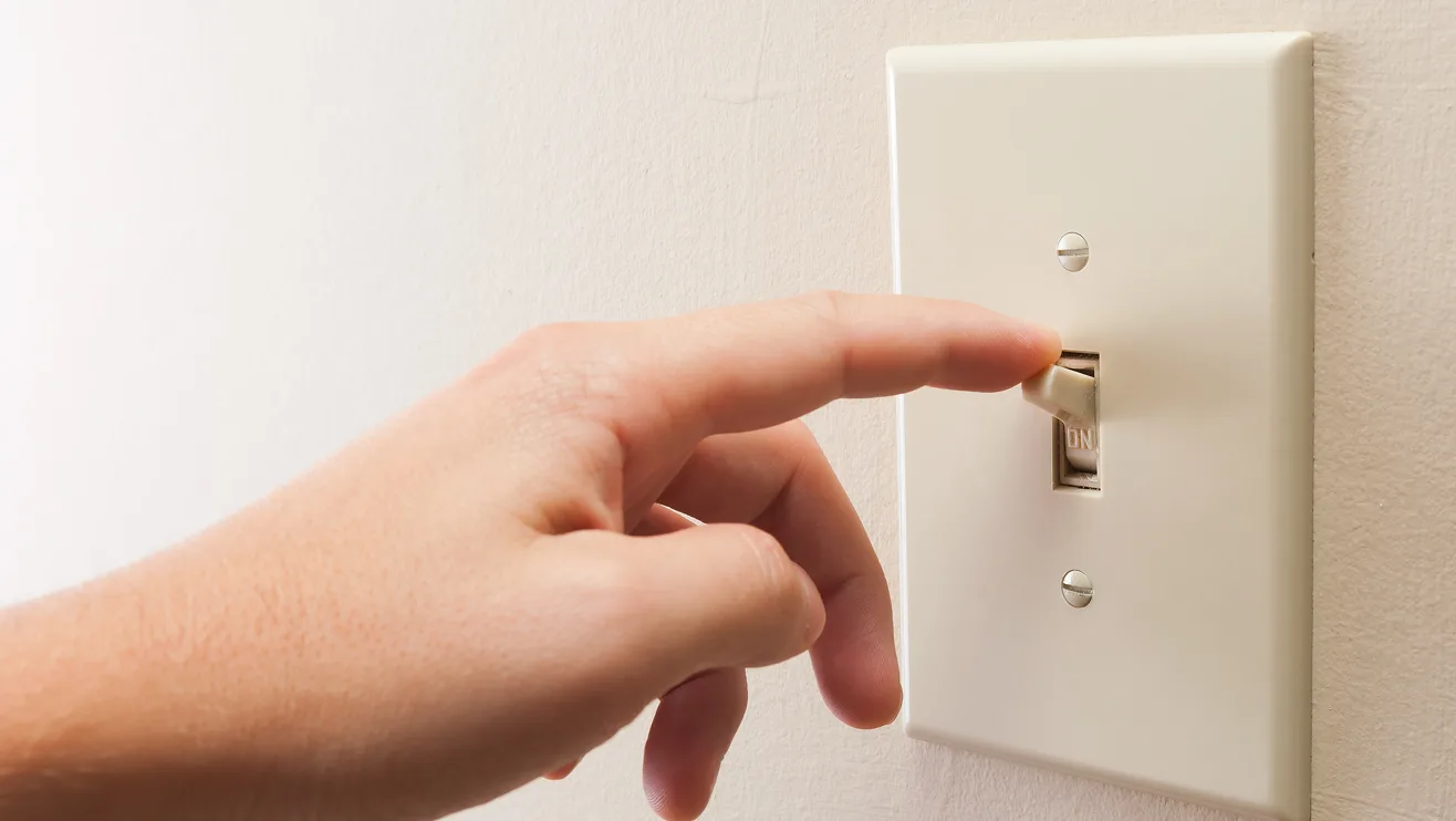 Hand reaching for light switch and finger placed on top of switch