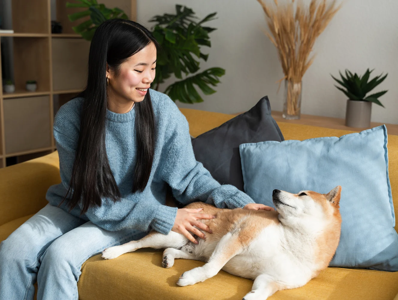Una mujer joven en un sofá en una sala de estar acariciando a un perro.