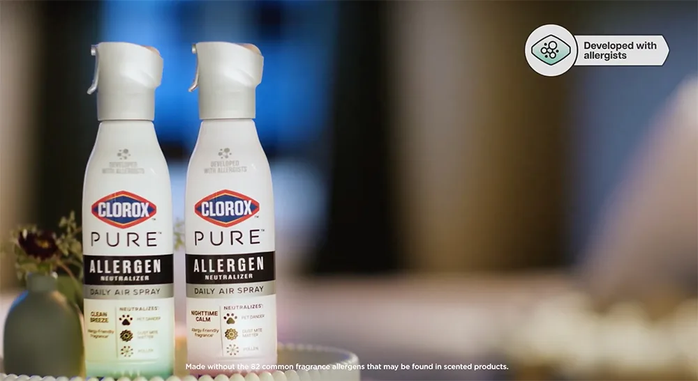 Two spray cans of PURE Allergen spray sitting on a table with a blurry background