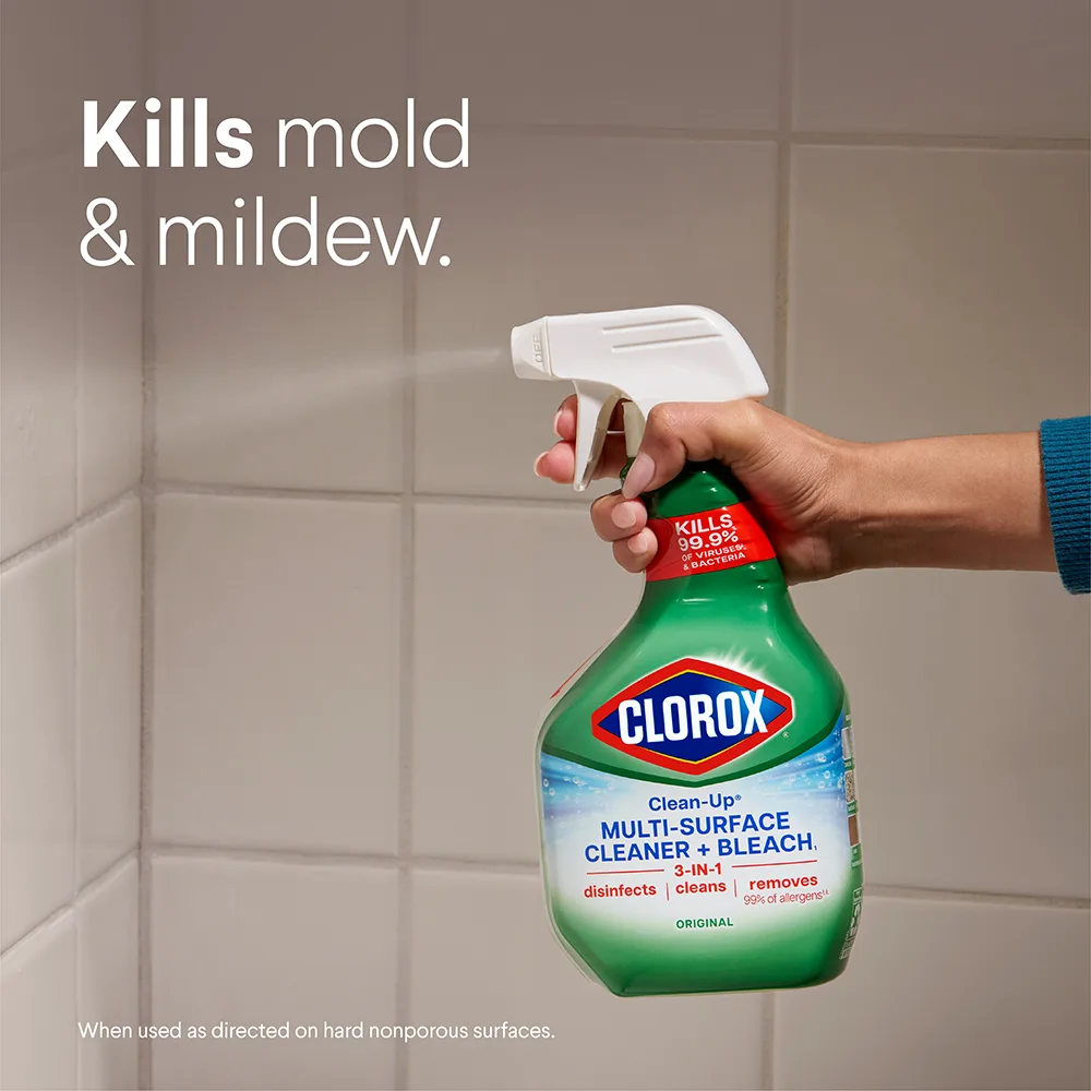 Person spraying Clean-Up spray on shower tiles with the words "Kills mold & mildew"