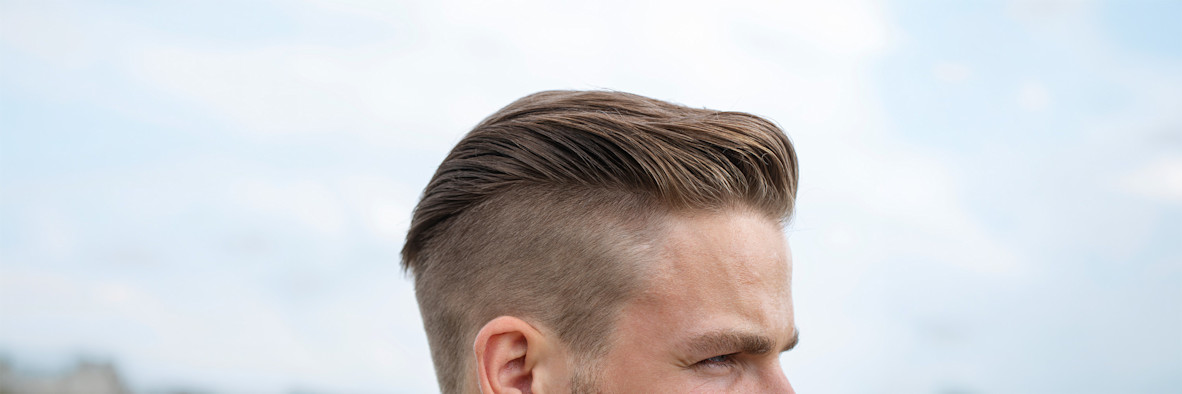 Side profile of a man with a sharp undercut fade haircut on a white background.