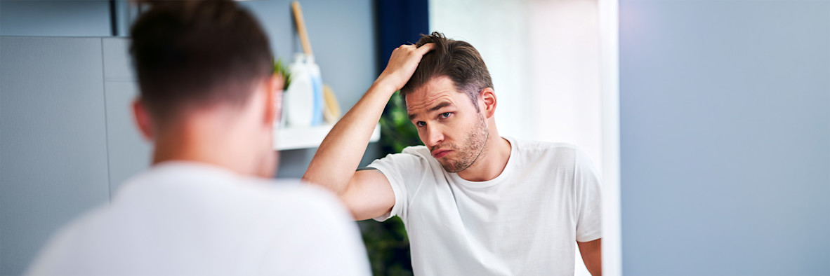 A man in a white t-shirt reaches up to touch or scratch his scalp.