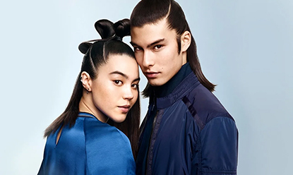 Young woman and young man both with long straight dark hair standing next to each other and looking at the camera.
